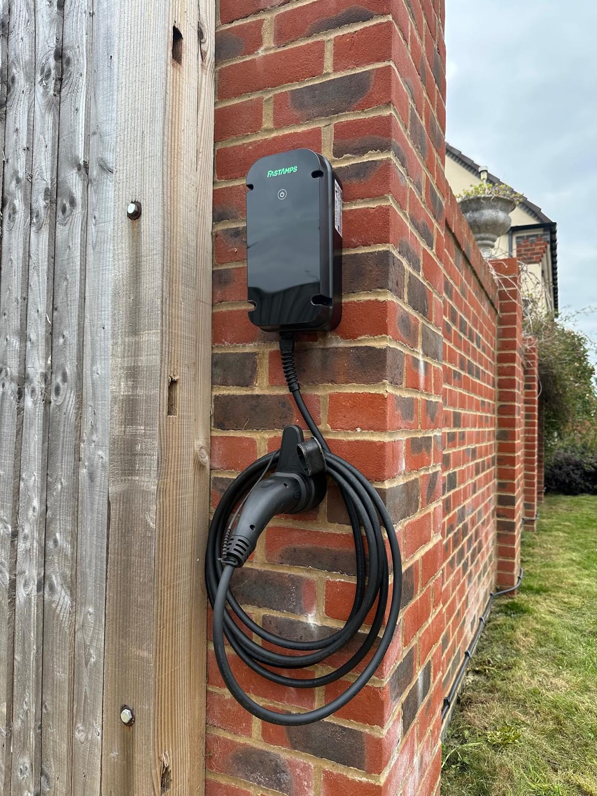 FastAmps EV charger installed on a brick garden wall, with the charging cable neatly coiled beneath