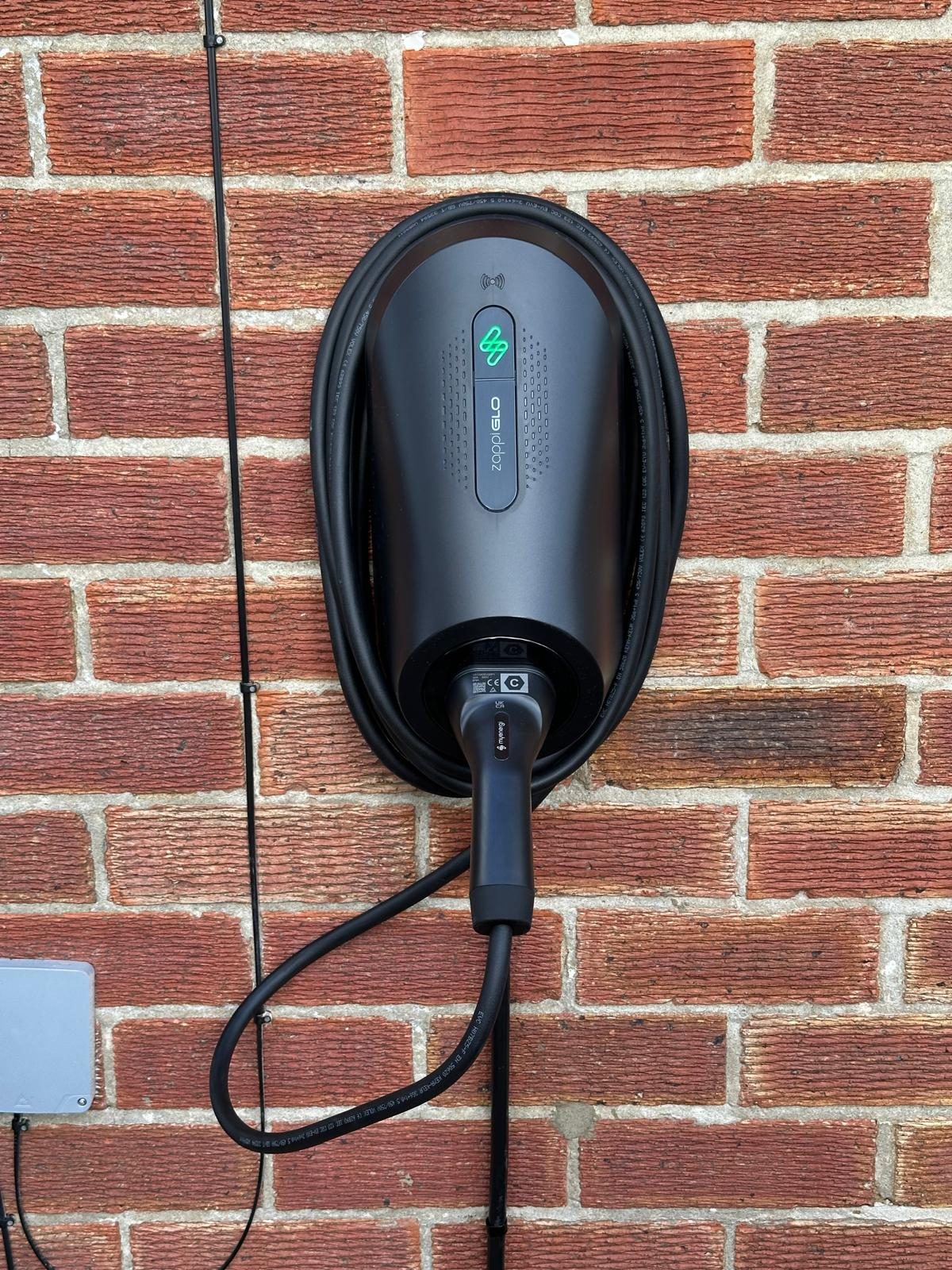 Myenergi Zappi GLO EV charger installed on a brick wall, cable coiled beneath